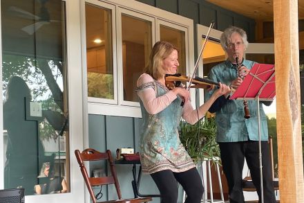 Orchestra musicians playing wind instruments indoors led by conductor.